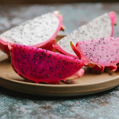 Ripe segments of dragon fruit with black seeds in colorful flesh served on round plate on gray table in kitchen on blurred background