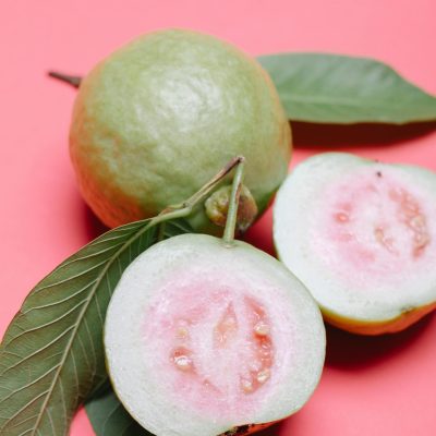 From above ripe fresh appetizing cut in half and whole fruits of guava on pink surface